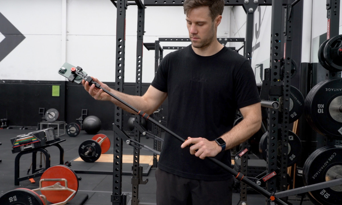 A strength training athlete extending their compact gym tripod to record bar speed with the Metric app